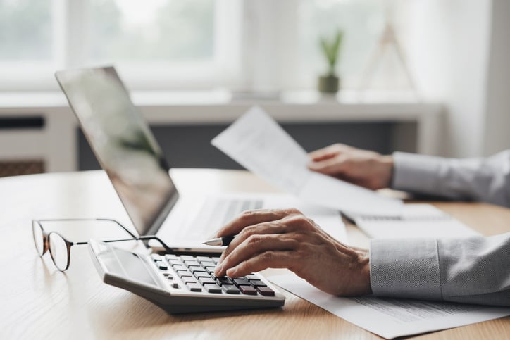 Man using calculator with computer laptop, budget and loan paper in office